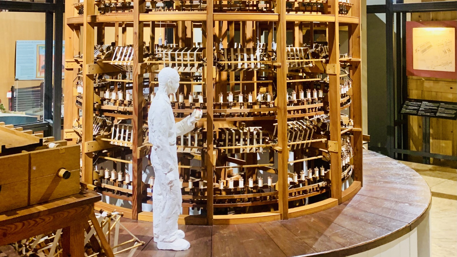 Wooden silk-spinning machine: cylindrical structure with several bobbins in each section. A mannequin in front of it shows it’s at least twice as tall as a person.
