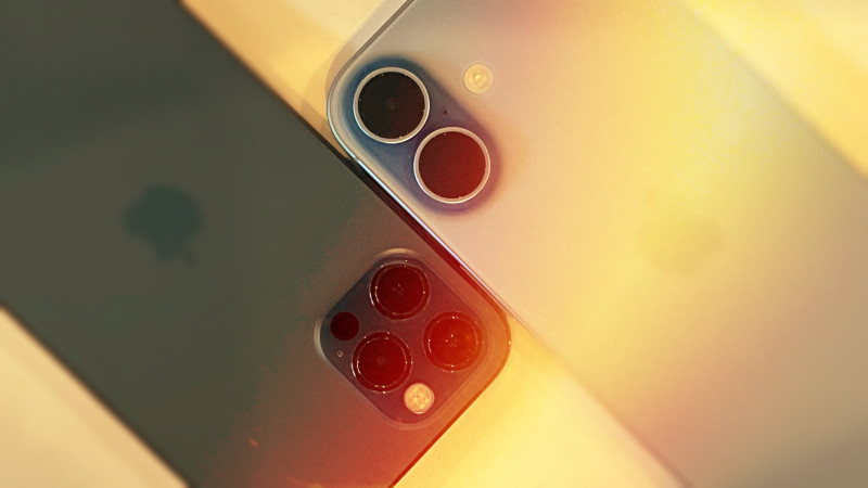 An iPhone 12 Pro (left) and an iPhone 17, both set face down, with their camera systems next to each other. The image has been edited with warm flare, reduced depth of field and color distortion