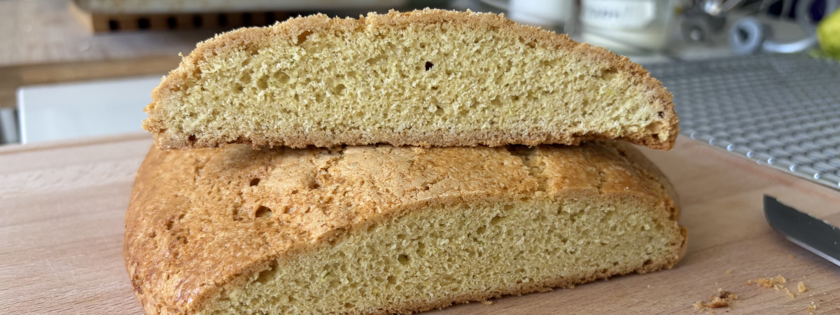 A flat loaf of baked brazadela (pâte sucrée cake) cut in half, one half on top of the other, with the cut end facing the viewer. The crust is crisp and lightly glazed with milk and sugar. The crumb is tight, with very small air bubbles
