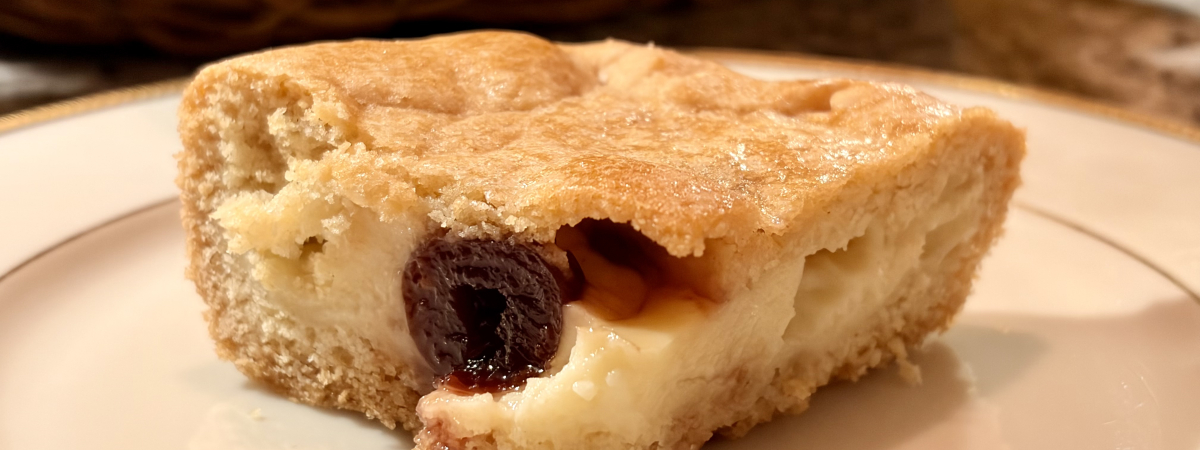 A square of custard tart with a half candied sour cherry in the middle